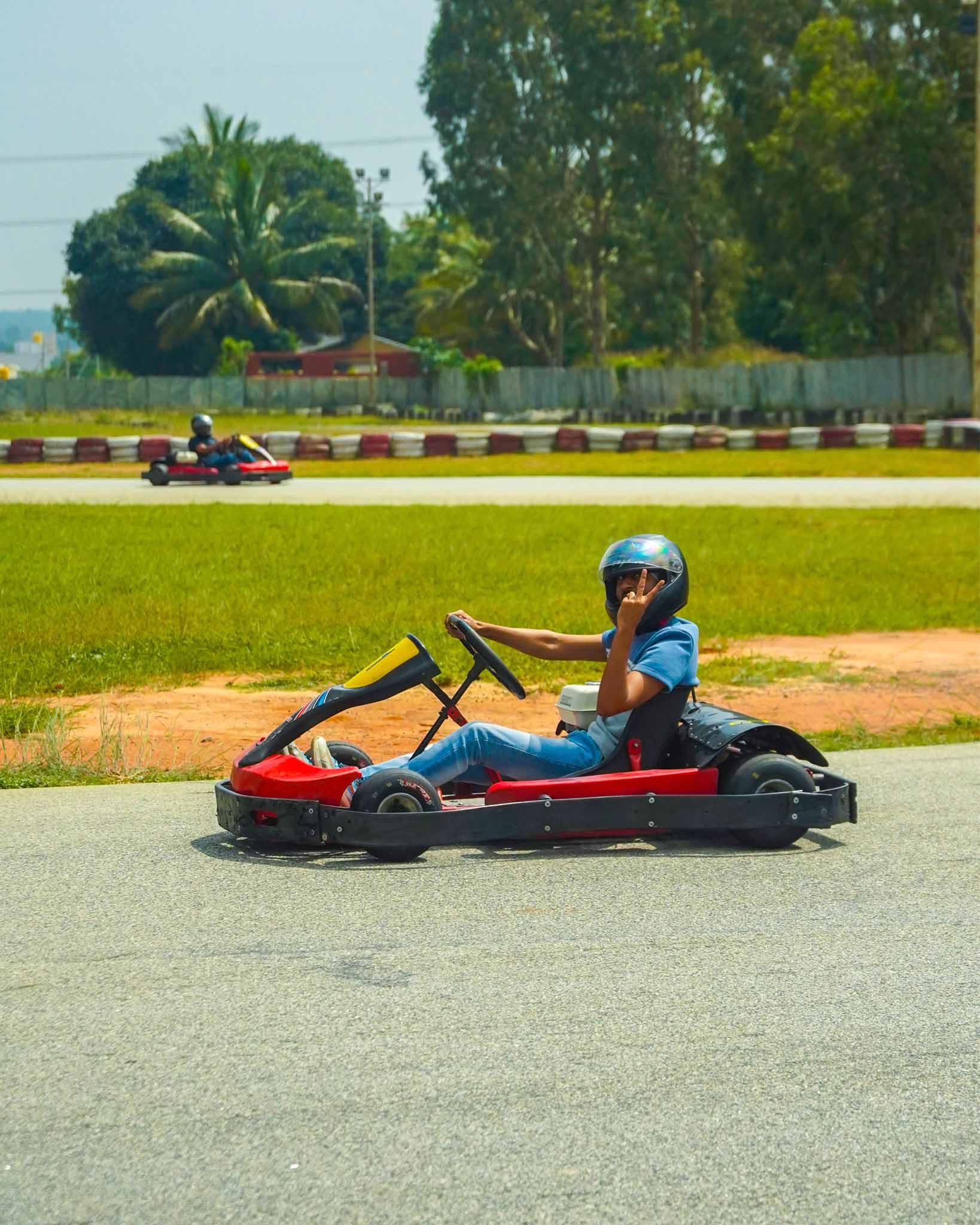 A driver in a go-kart waving while taking a turn on the track.